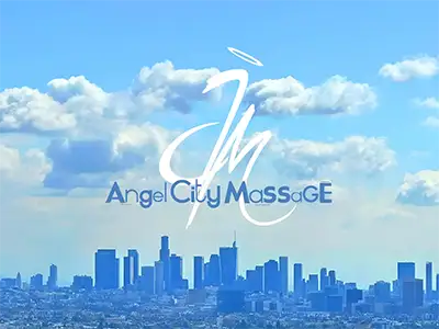 A woman receiving a relaxing facial massage from ACM mobile massage services while lying down with eyes closed. Her head is adorned with small pink and white flowers, resting on a white towel. A pink towel covers her shoulders.